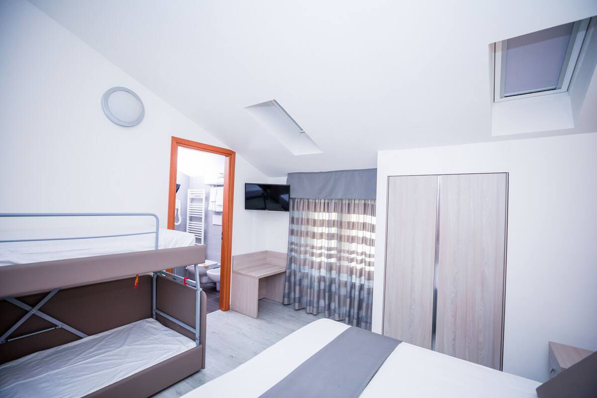 A modern hotel room with bunk beds, a desk, a TV, and a wardrobe.