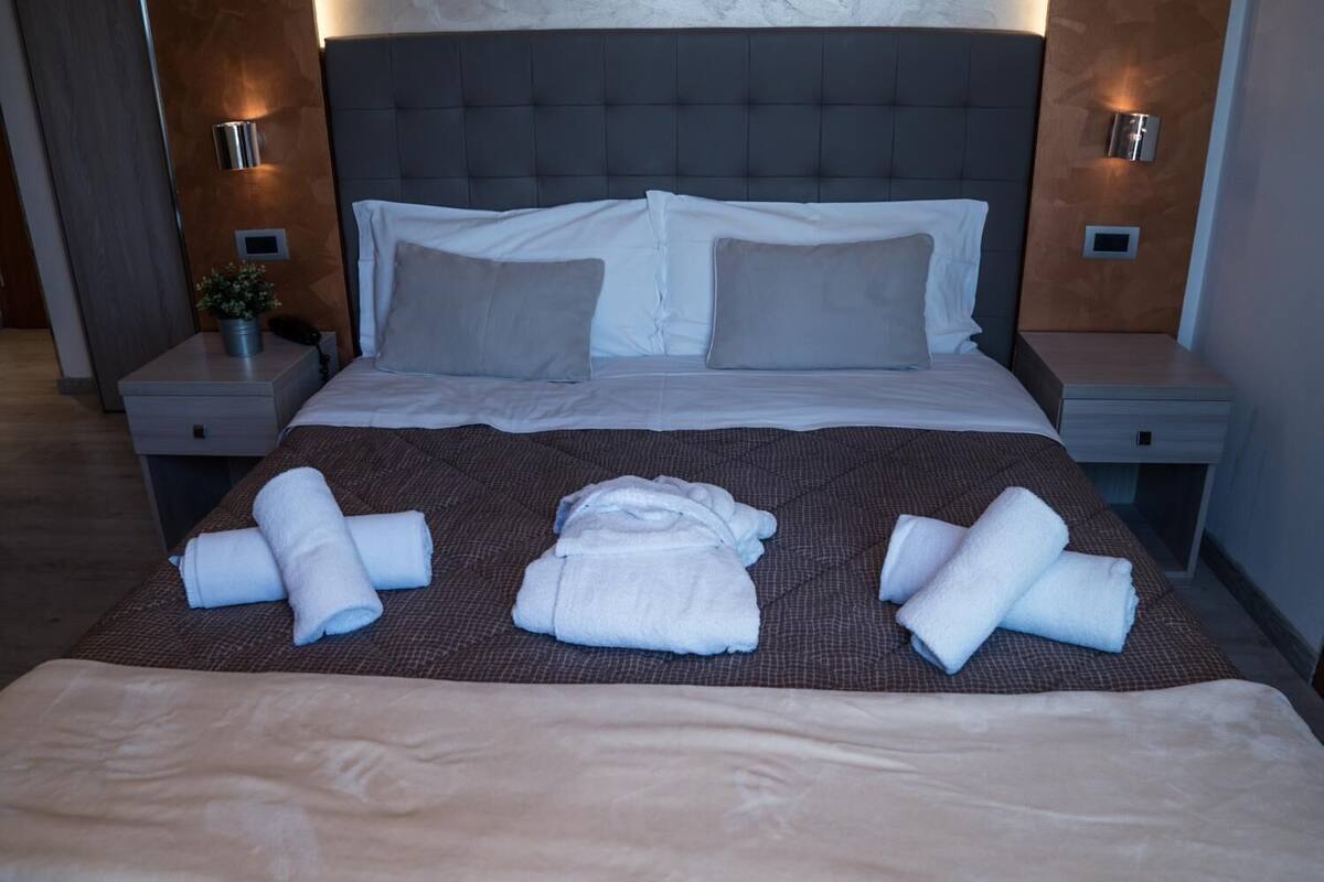 A neatly made bed with a dark headboard, two bedside tables with lamps, and a potted plant on one table.