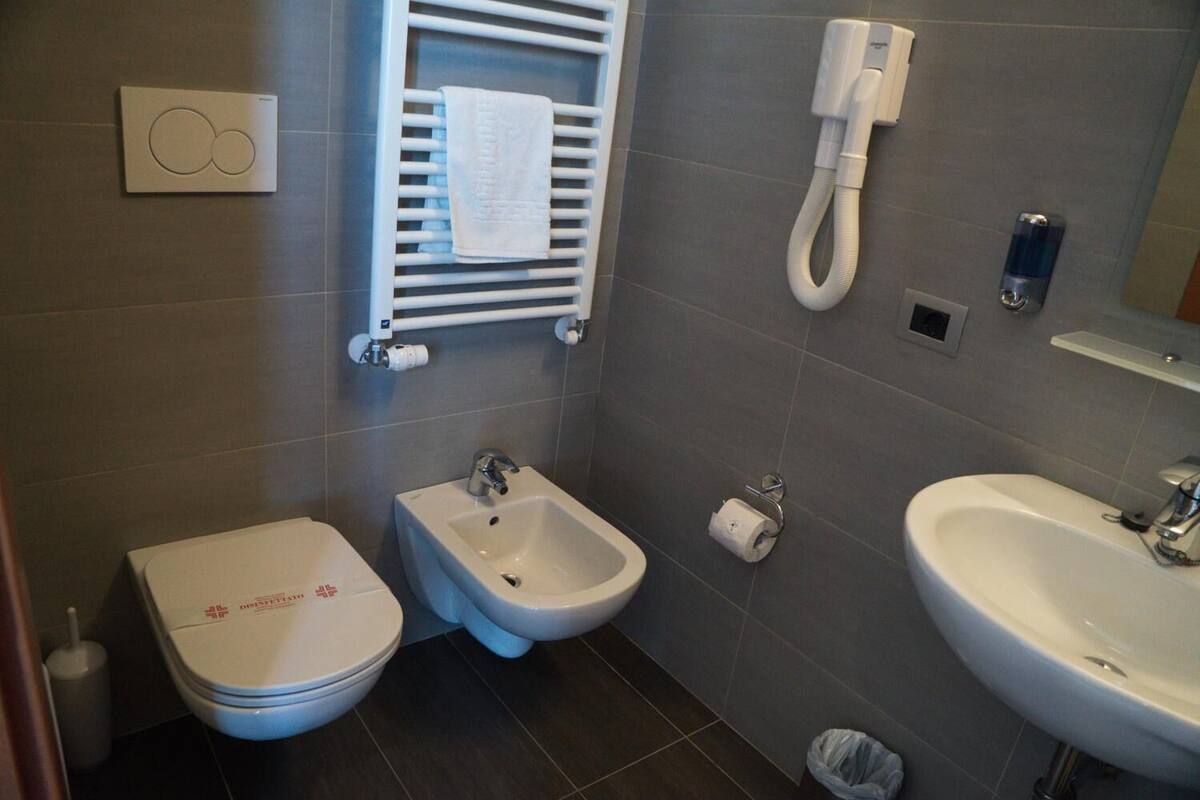 A bathroom with a toilet, bidet, and sink, a towel rack, a toilet paper holder, and a hand dryer.