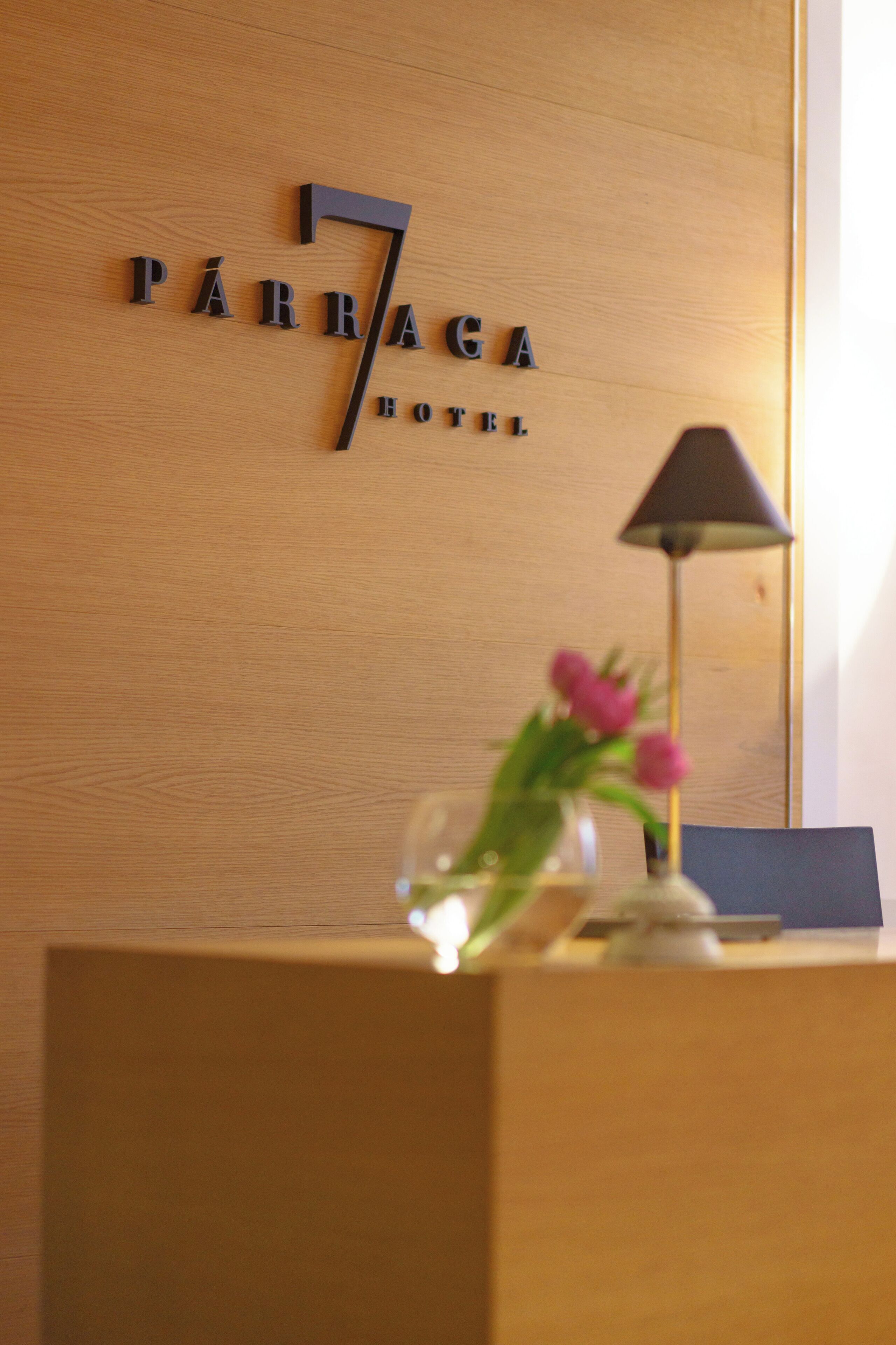 A wooden reception desk with a sign reading "PÁRRAGA HOTEL" and a lamp with pink flowers.