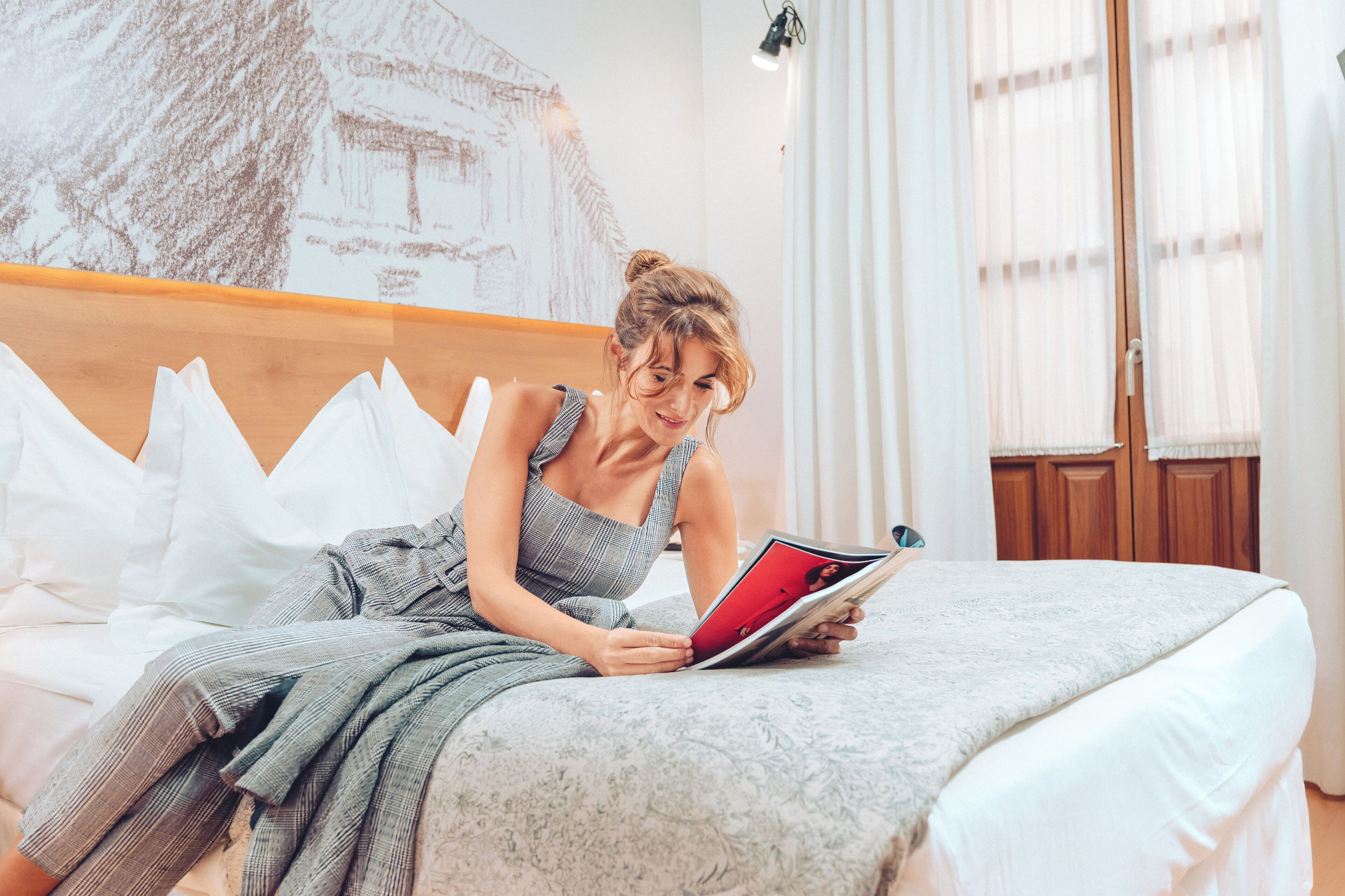 Una persona sentada en una cama con una colcha grande, leyendo una revista.