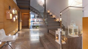 A modern hotel lobby with a glass staircase, a reception desk, and a bar area in the background.