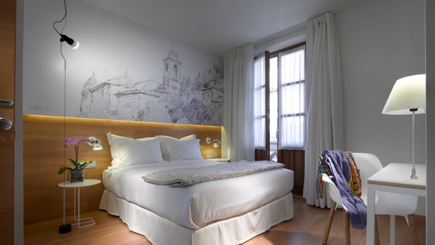 A modern bedroom with a large bed, a bedside table with a lamp, a chair, and a wall mural.