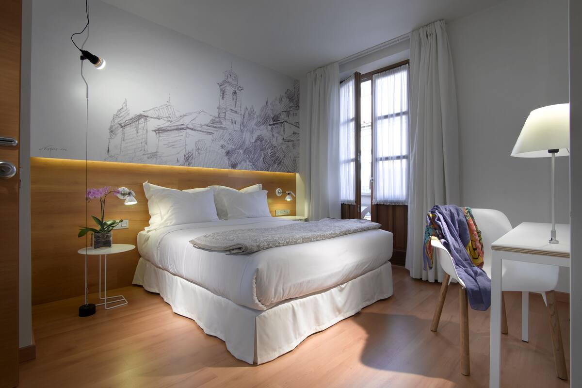 A modern bedroom with a large bed, a bedside table with a lamp, a chair, and a wall mural.