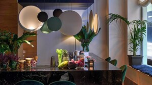 A modern dining area with a marble countertop, green upholstered chairs, and a variety of fruits and plants on the table.