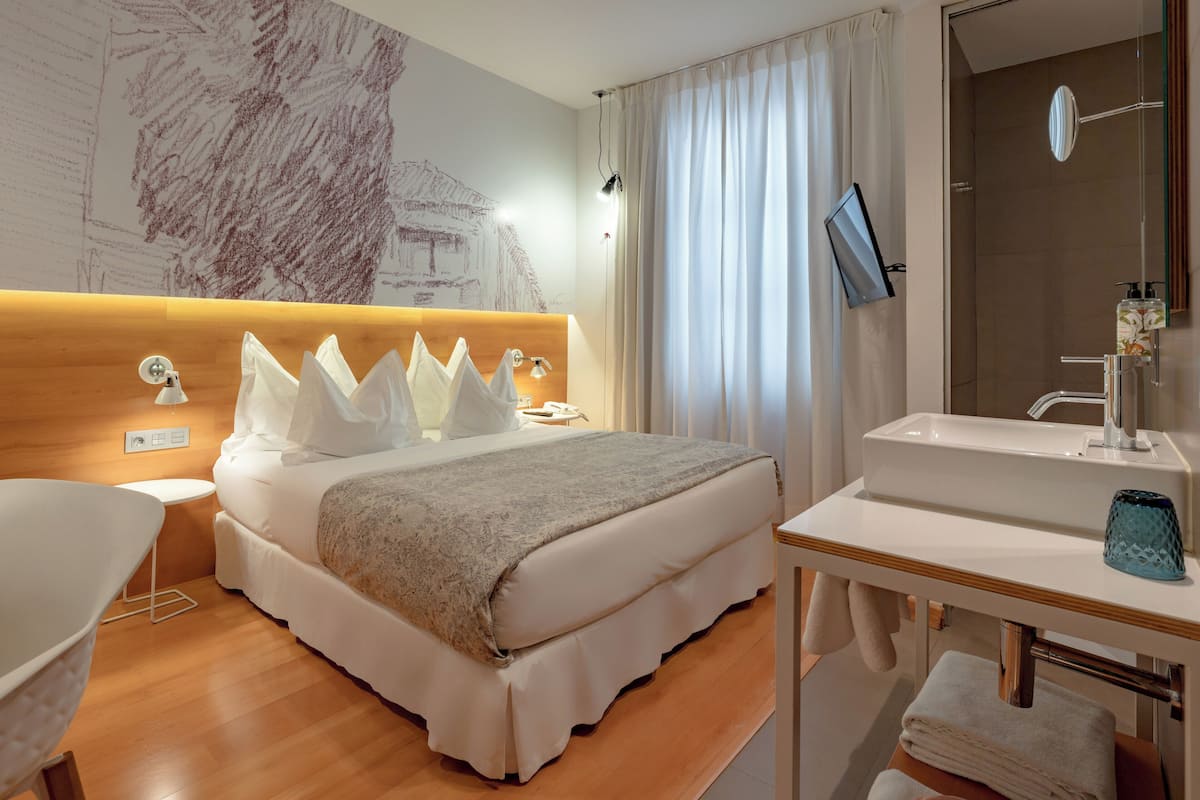 A hotel room with a large bed, bedside tables, a desk with a sink, a mirror, and a shower area.