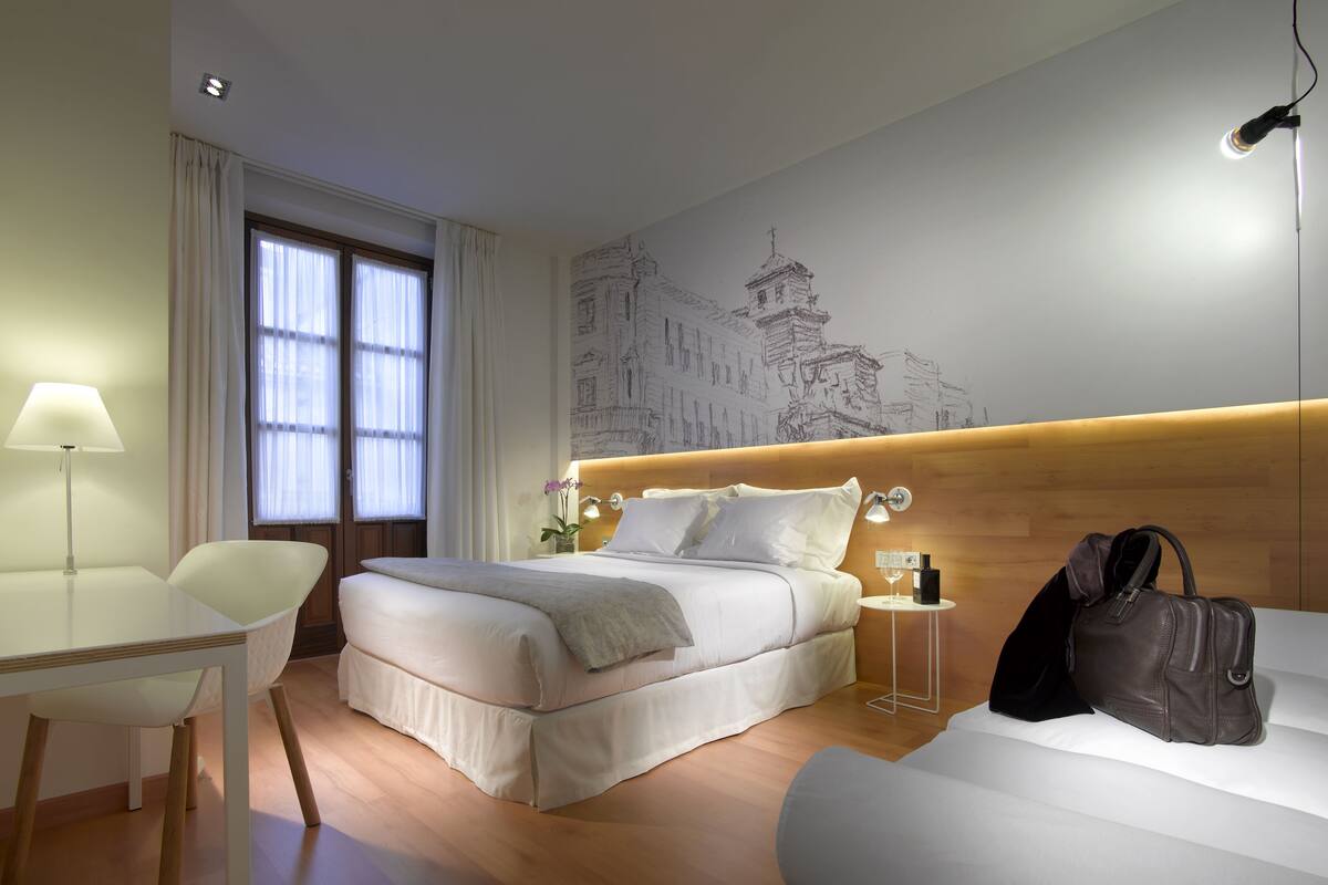 A hotel room with a bed, bedside table, lamp, and a wall with a cityscape mural.
