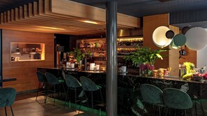 A modern bar area with a wooden accent wall, a marble countertop, and green upholstered bar stools.