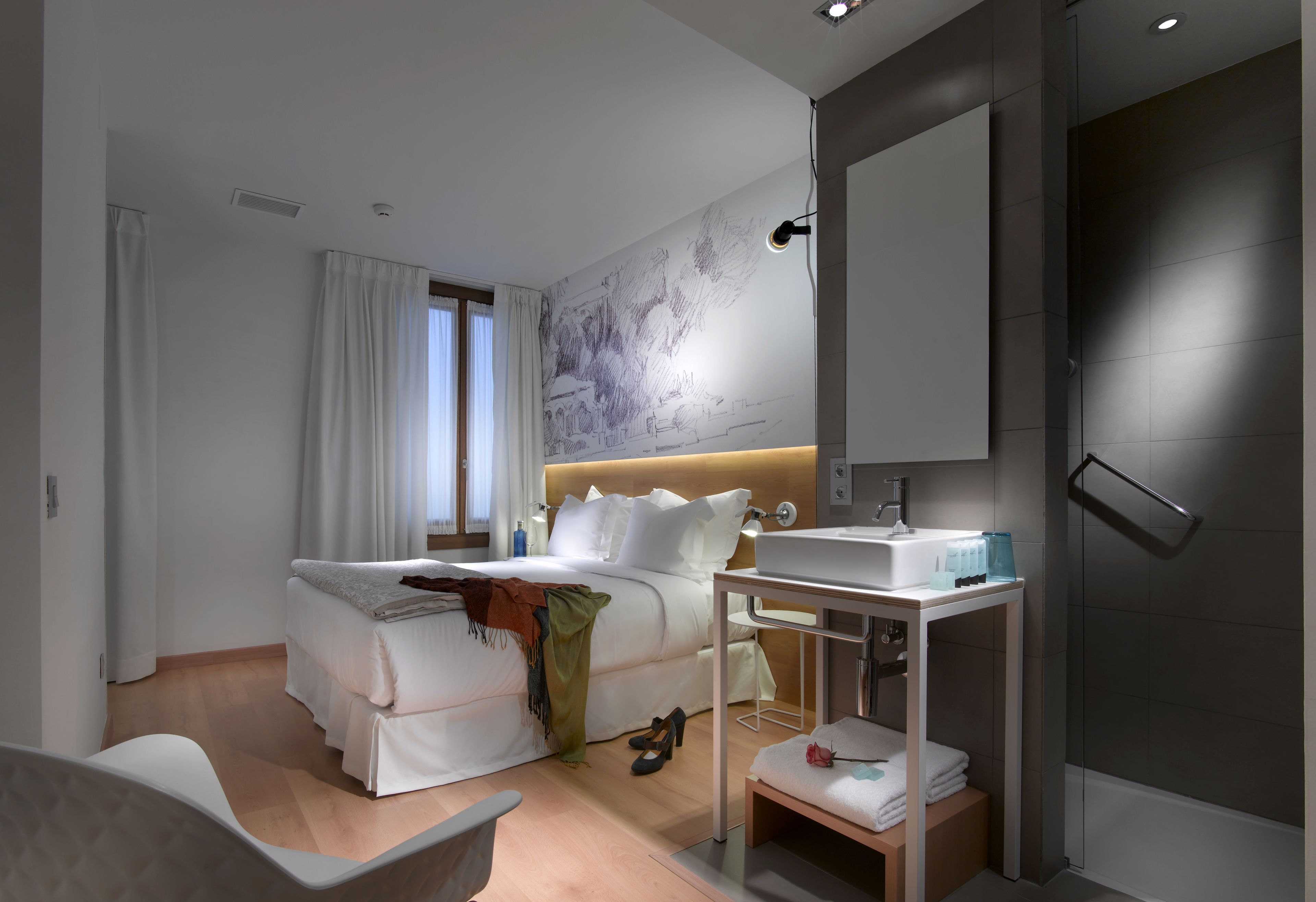A modern hotel room with a bed, bedside table, and a shower area.