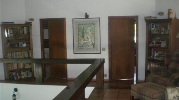 A room with a wooden staircase, a plaid armchair, and a bookshelf filled with books. - Pousada do Golfista (Guaruja)