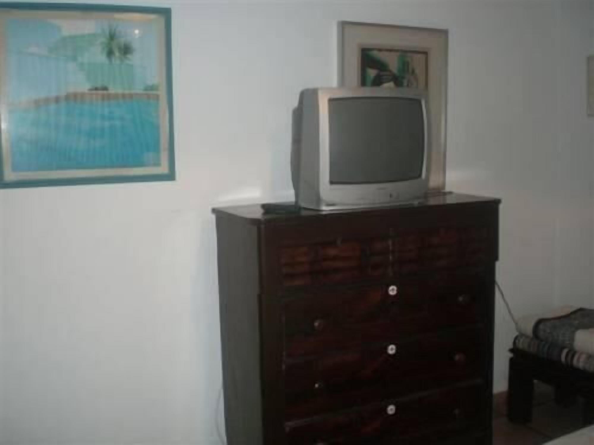 Ein Zimmer mit einem Holzkoffer, einem Fernseher darauf und einem gerahmten Bild an der Wand.