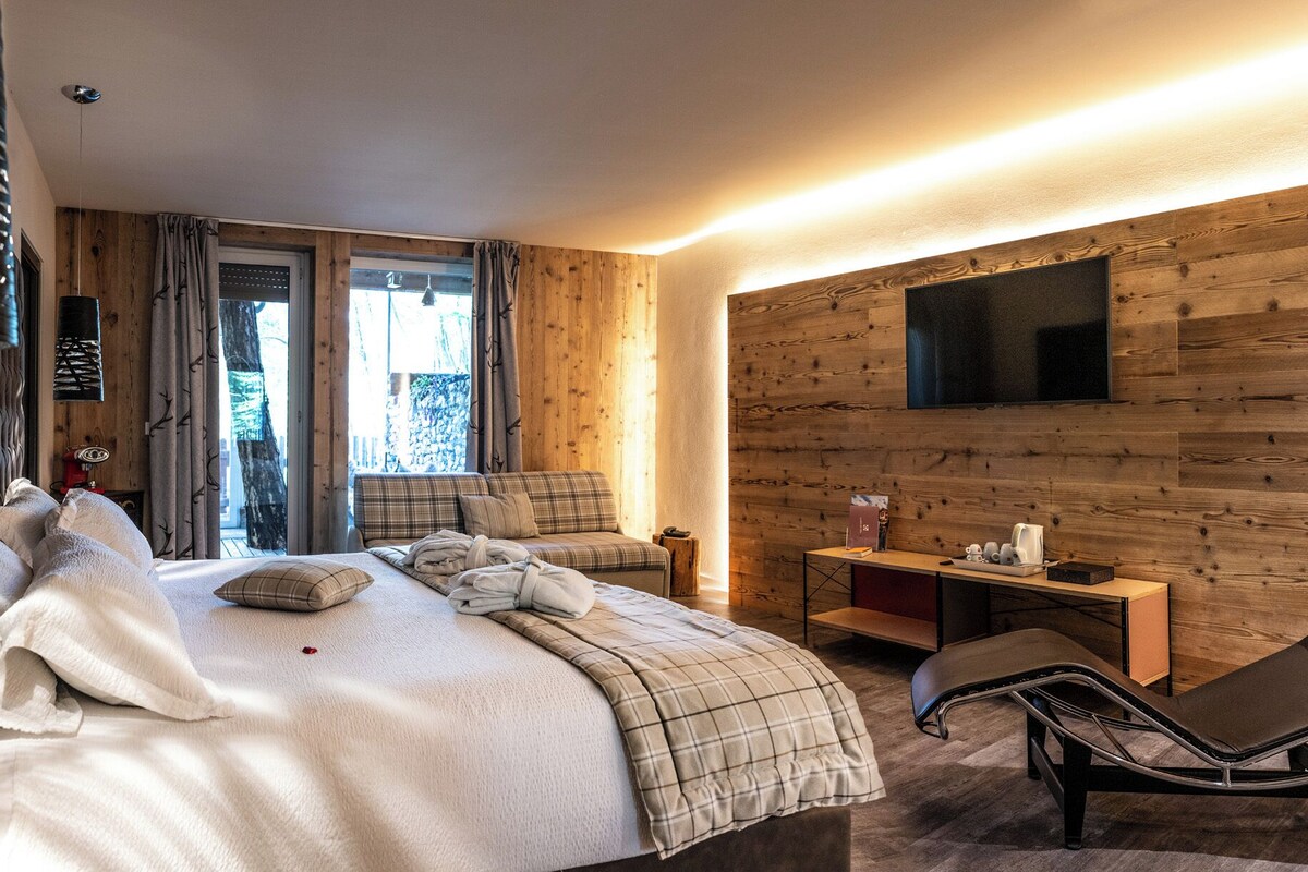 Ein modernes Hotelzimmer mit einem großen Bett, einer Sitzecke, einem an der Wand montierten Fernseher und einer Holzpaneel-Wand.