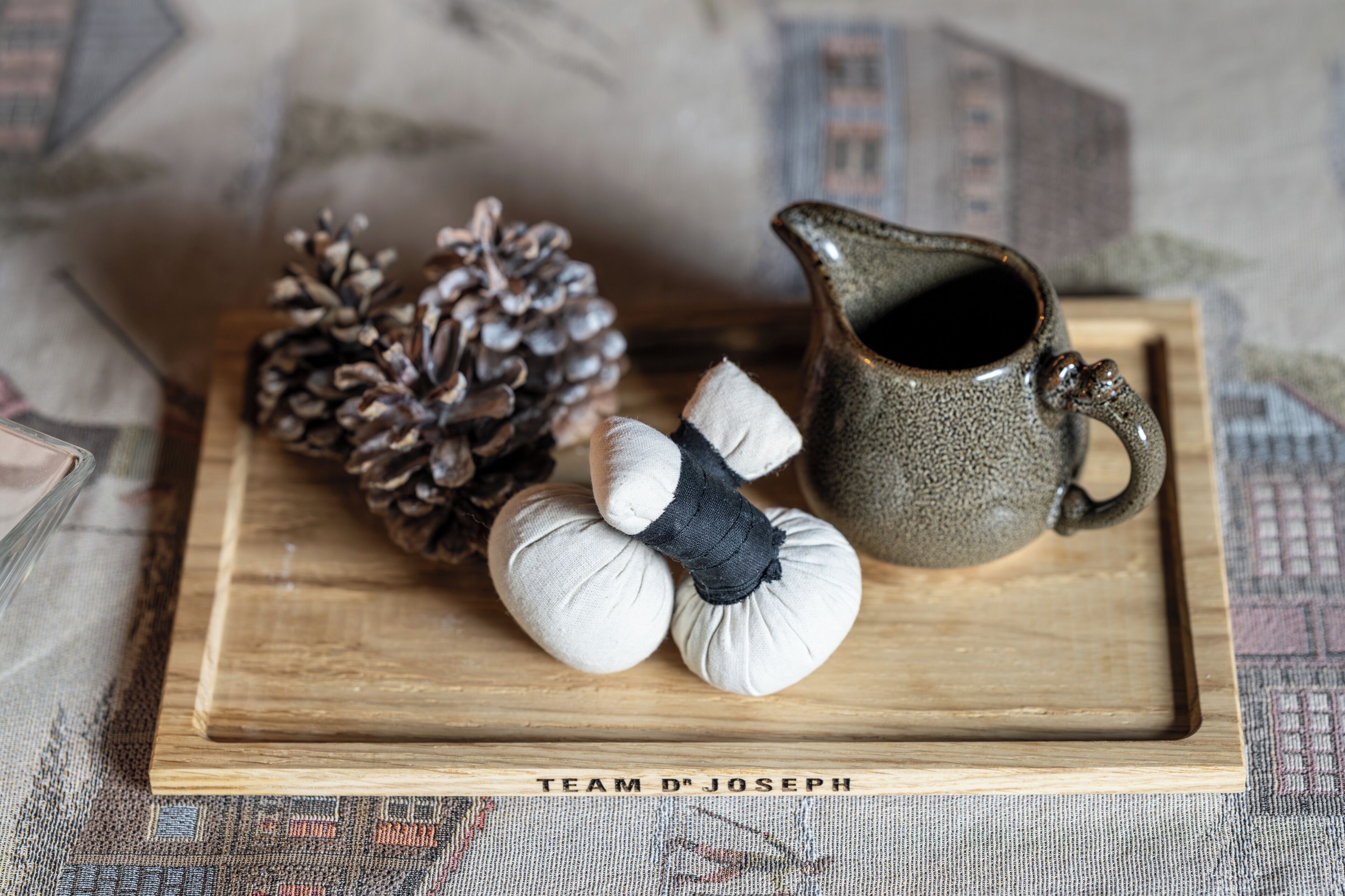 A wooden tray with a ceramic pitcher, pine cones, and fabric items.
