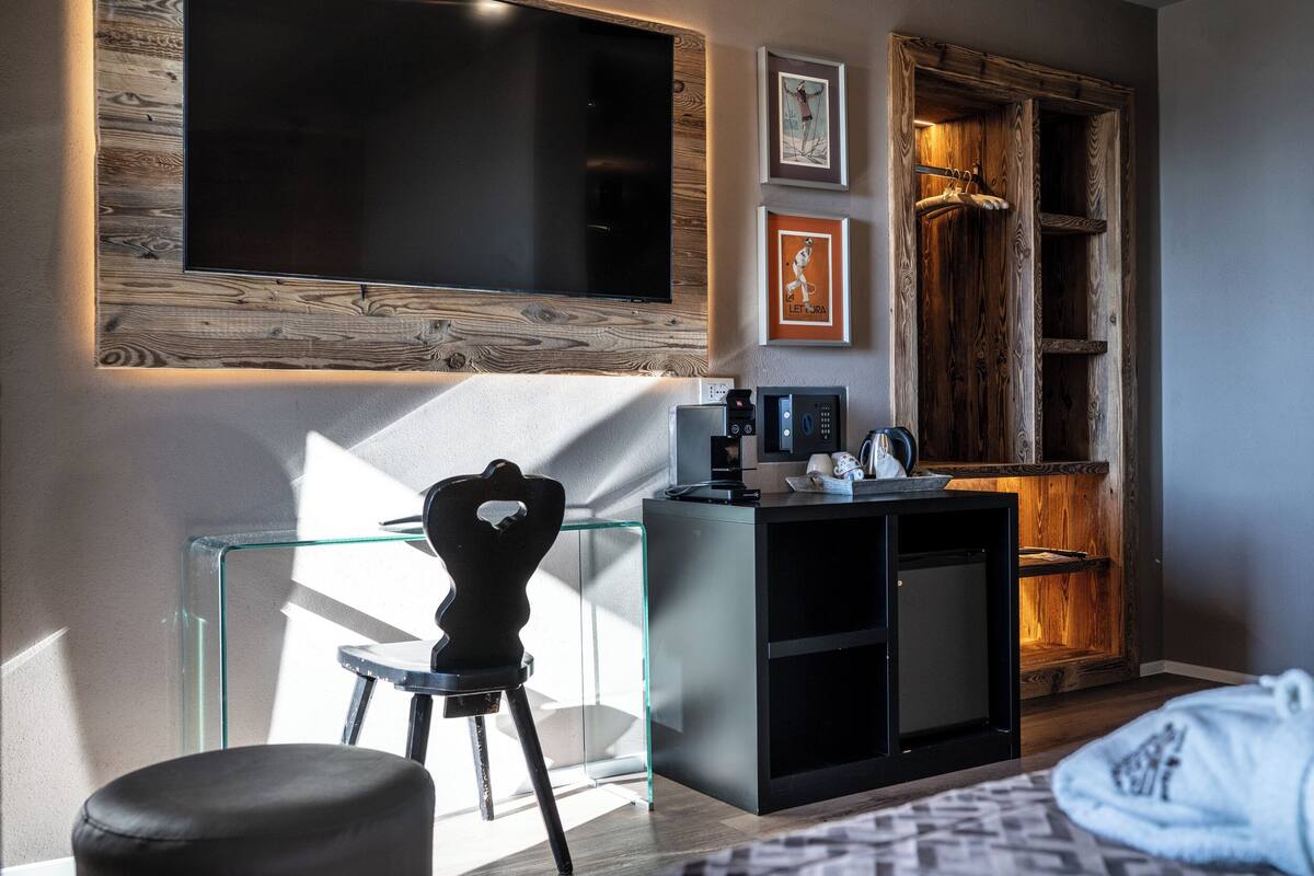 Une chambre moderne dotée d’un grand téléviseur à écran plat, d’un bureau en verre, d’une chaise noire, d’une armoire en bois et d’œuvres d’art encadrées accrochées au mur.