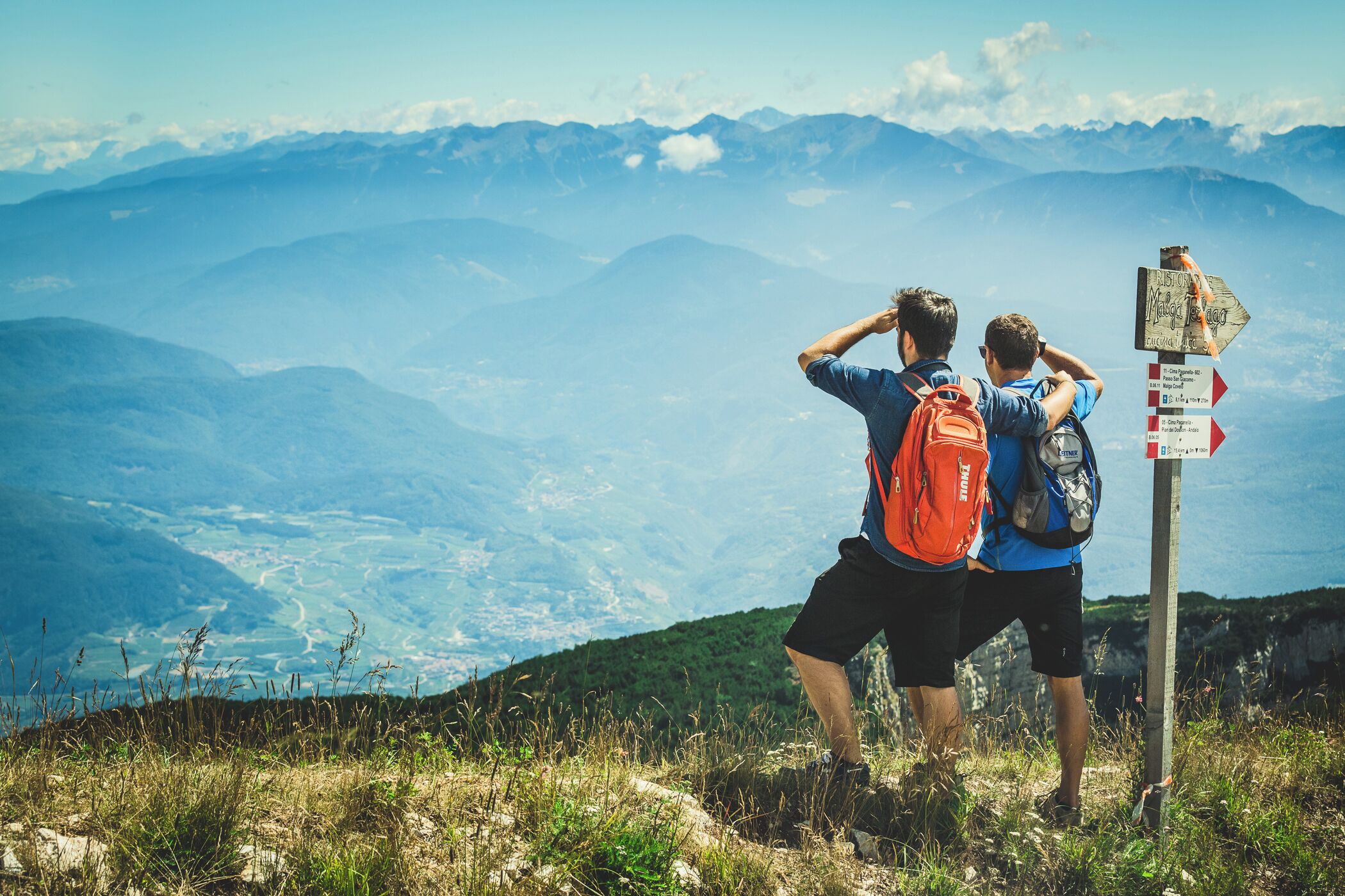 Two people standing on a mountain with a signpost in the foreground.