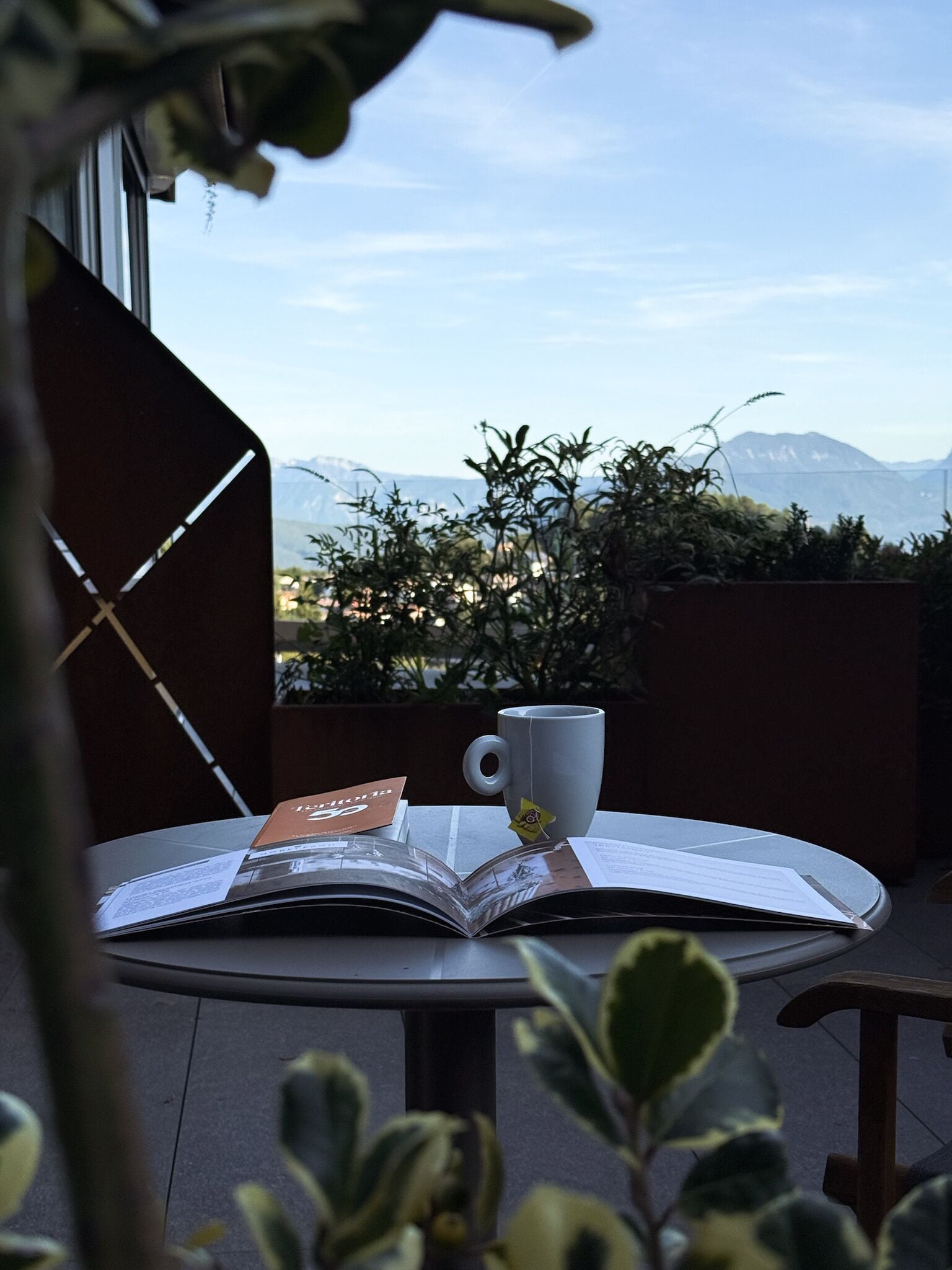 Ein Tisch mit einem Buch und einer Tasse auf einem Balkon mit Blick auf Berge.