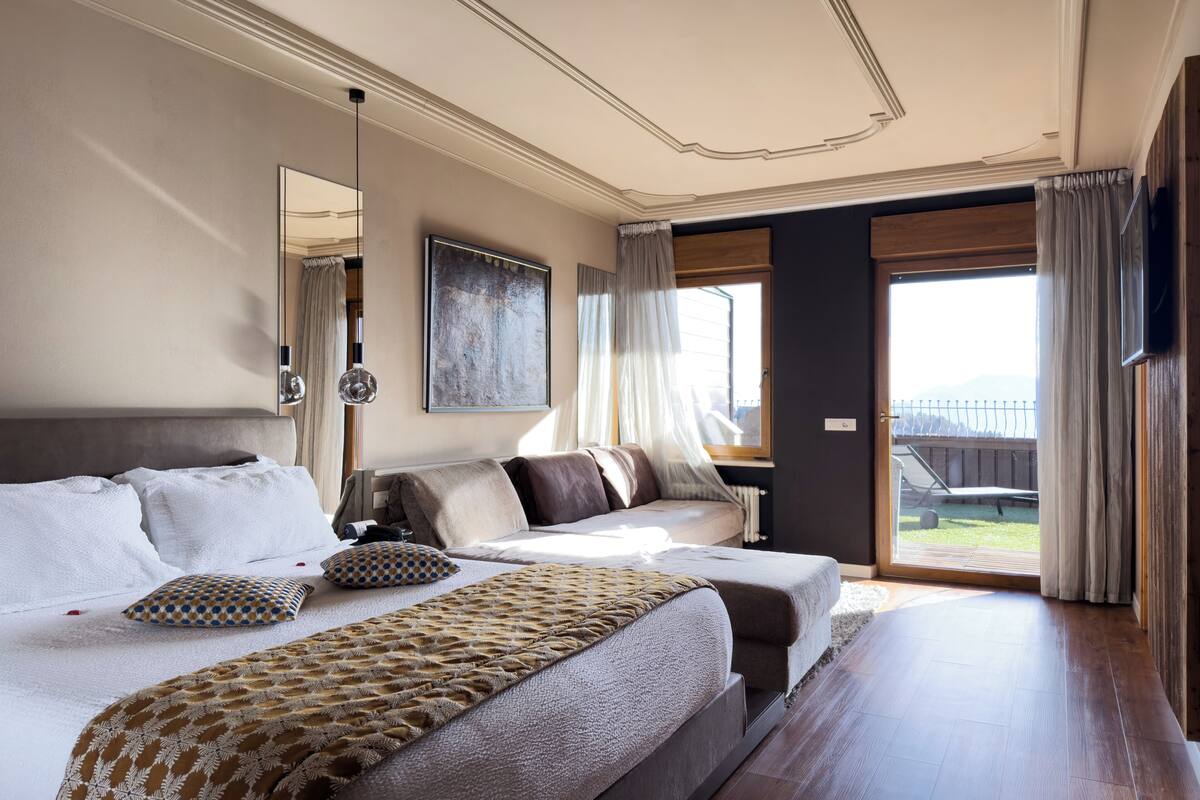 Une chambre spacieuse avec un grand lit, un coin salon, une fenêtre avec des rideaux et une vue sur l’extérieur.
