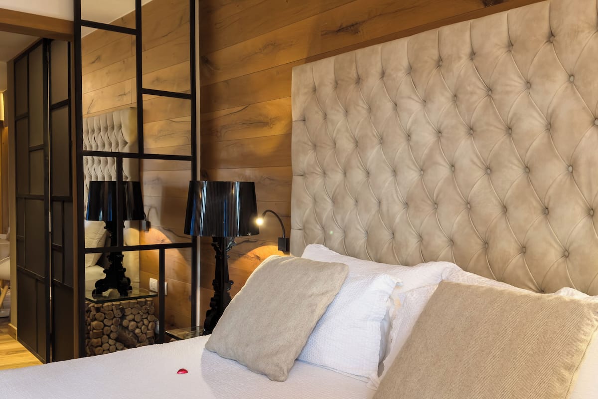 Une chambre à coucher avec une tête de lit capitonnée, un lit recouvert de draps blancs et une table de chevet avec des lampes.