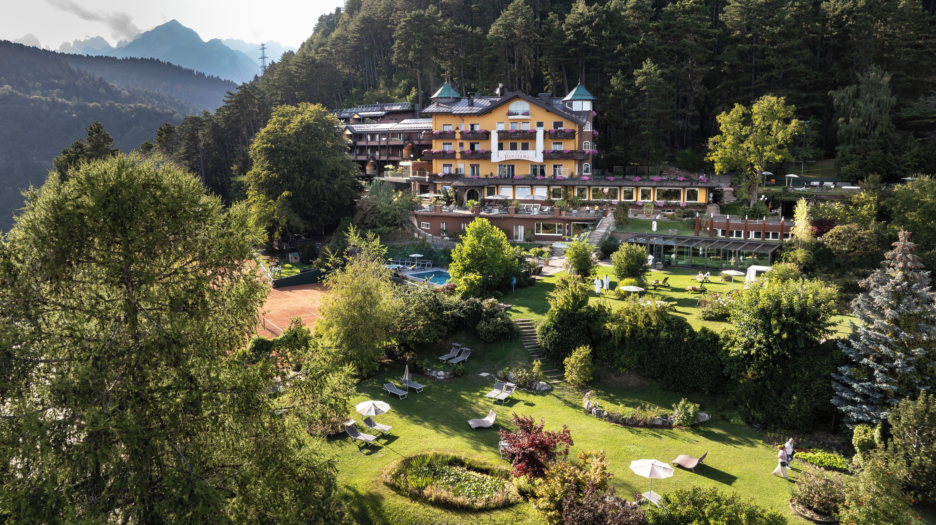 A hotel with multiple balconies, a swimming pool, and a well-maintained garden.