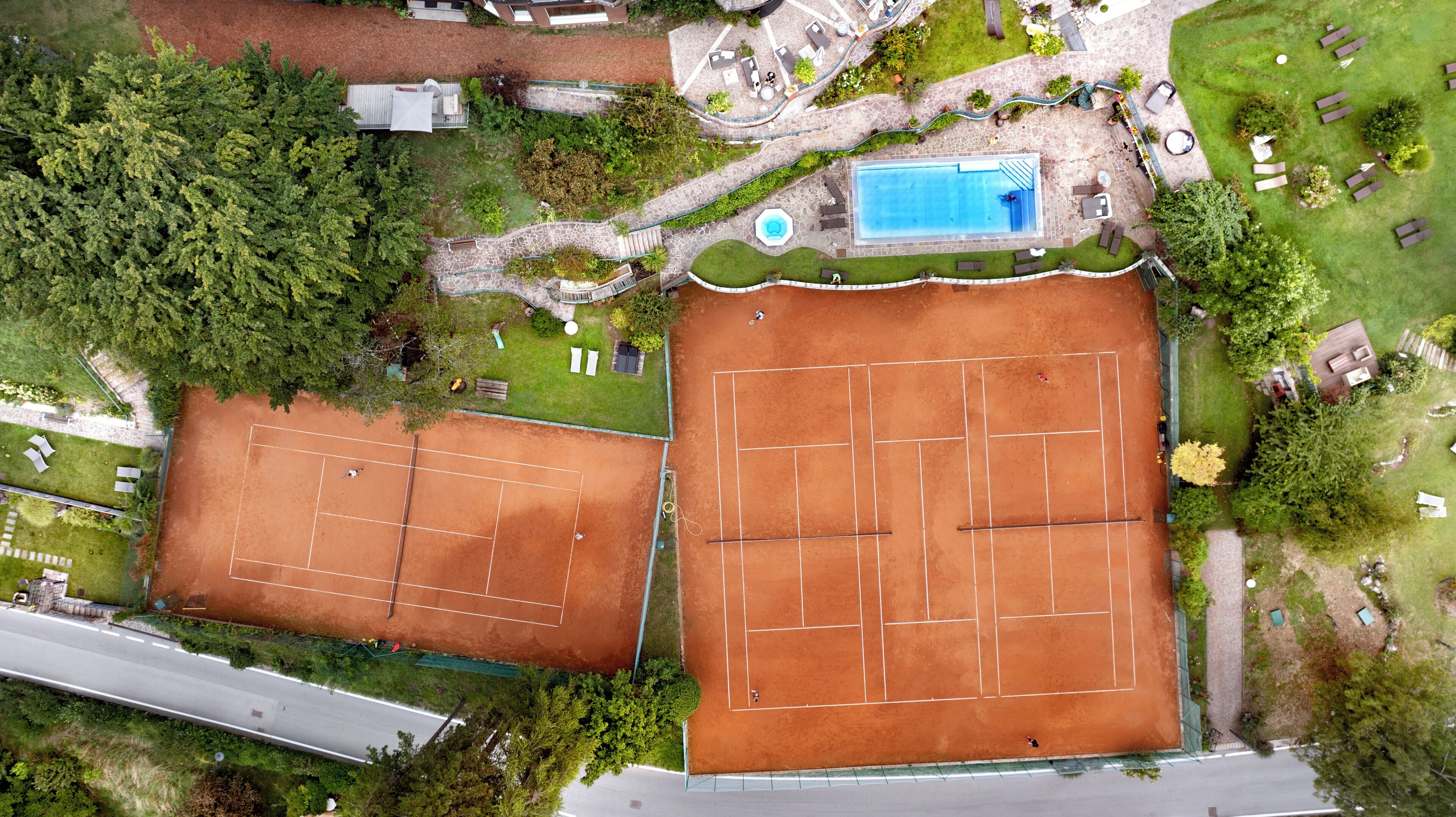 Vista aérea de una propiedad con dos canchas de tenis, una piscina y abundante vegetación.