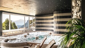 Een hottub met houten ligbedden en een stenen muur, met uitzicht op een bergachtig landschap.