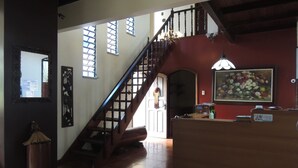 Un espace d’accueil avec un escalier en bois, un comptoir de réception, un tableau et un grand miroir.