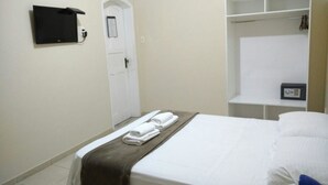 Une chambre d’hôtel avec un lit, une armoire, un téléviseur fixé au mur et une porte.