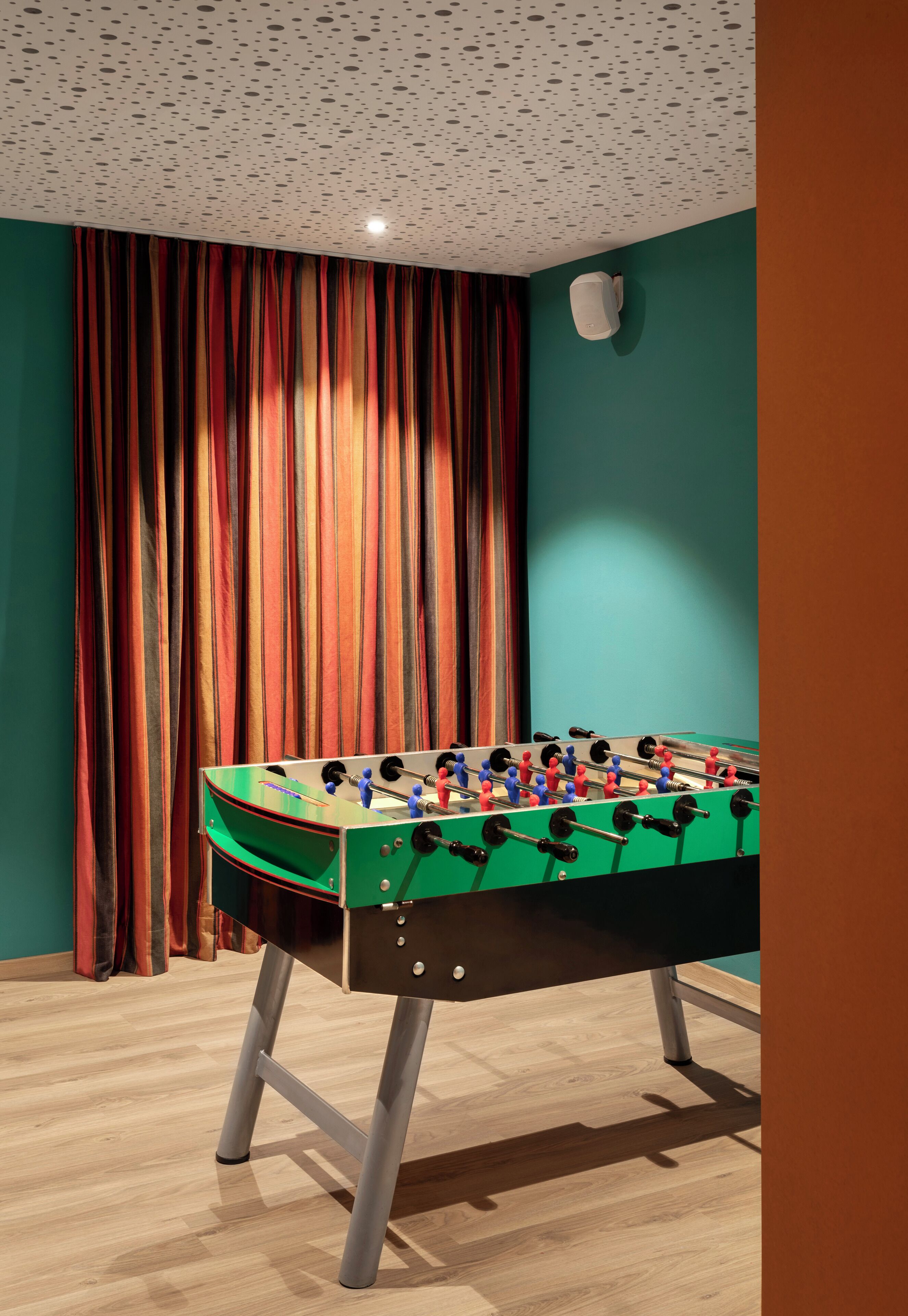 Una mesa de fútbol de mesa en una habitación con paredes verde agua y suelo de madera.