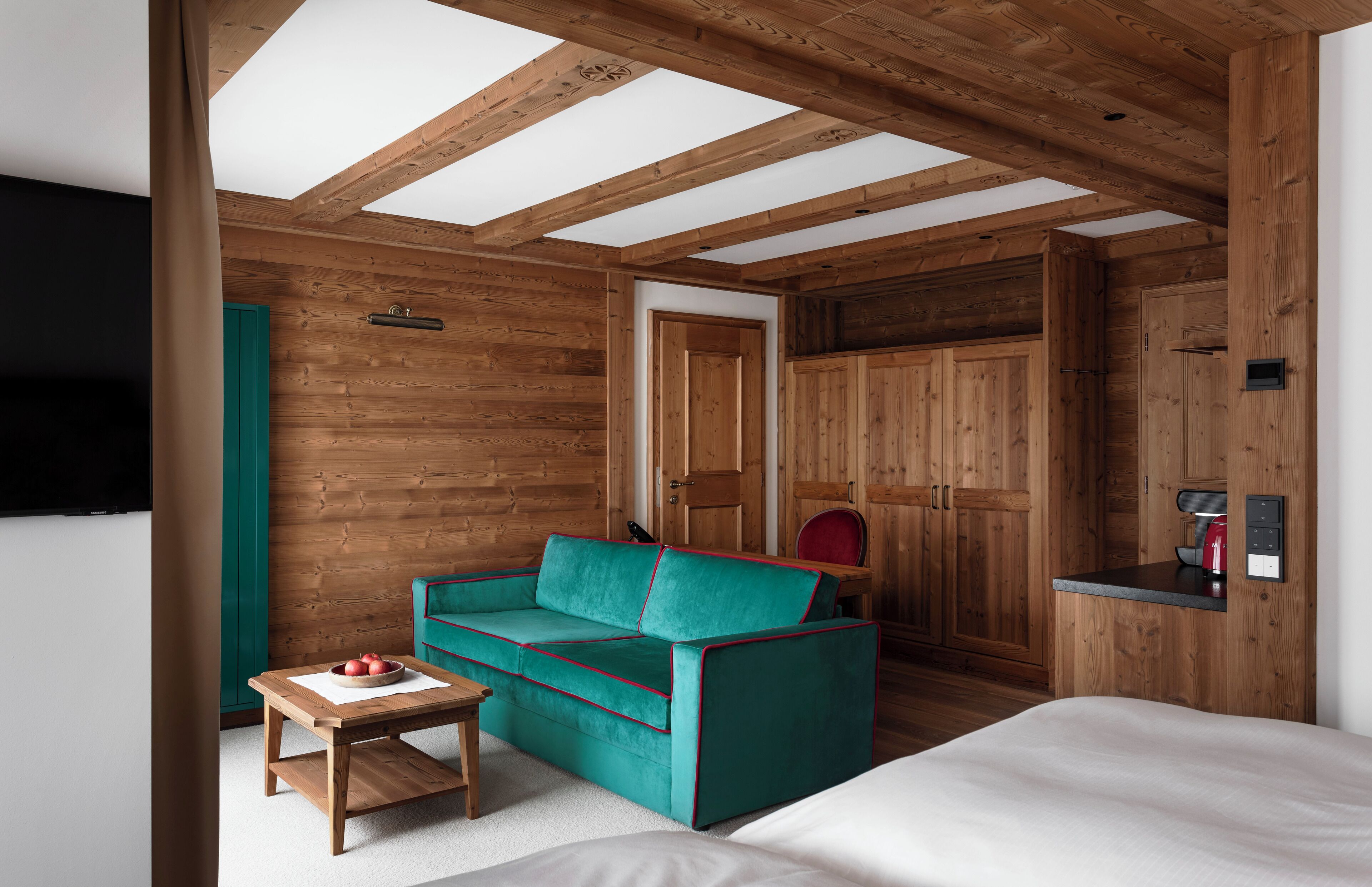 Une pièce chaleureuse avec un plafond en bois, un canapé de couleur turquoise, une petite table en bois et un lit.