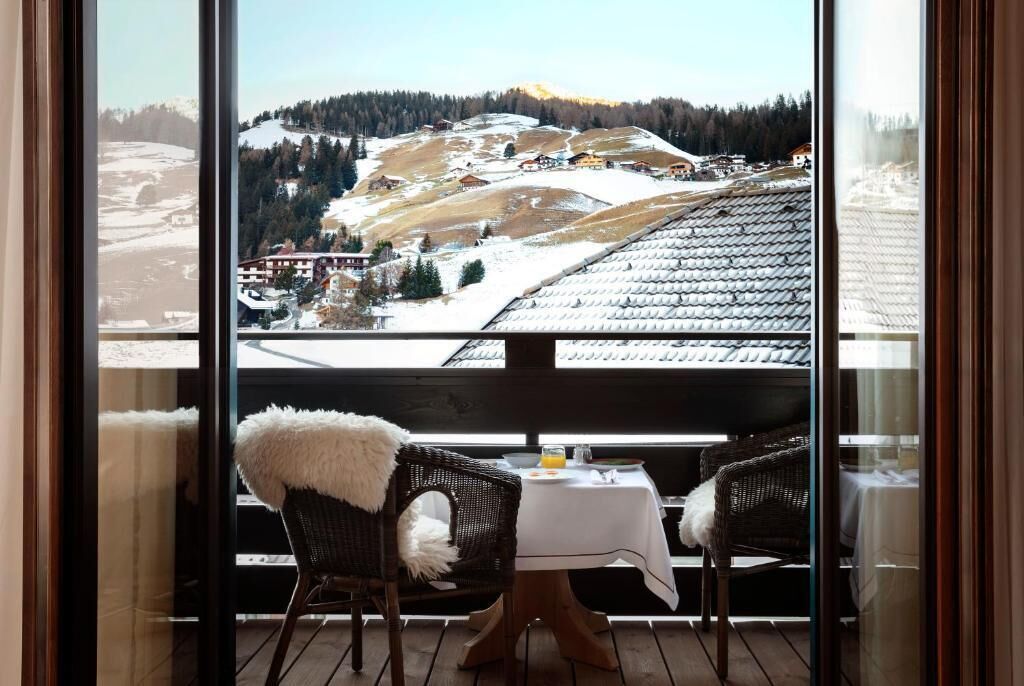A balcony with a view of a snowy mountain landscape, a wicker chair with a fur throw, and a table with a white tablecloth.