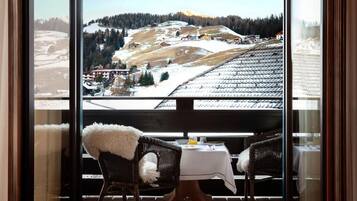 A balcony with a view of a snowy mountain landscape, a wicker chair with a fur throw, and a table with a white tablecloth.
