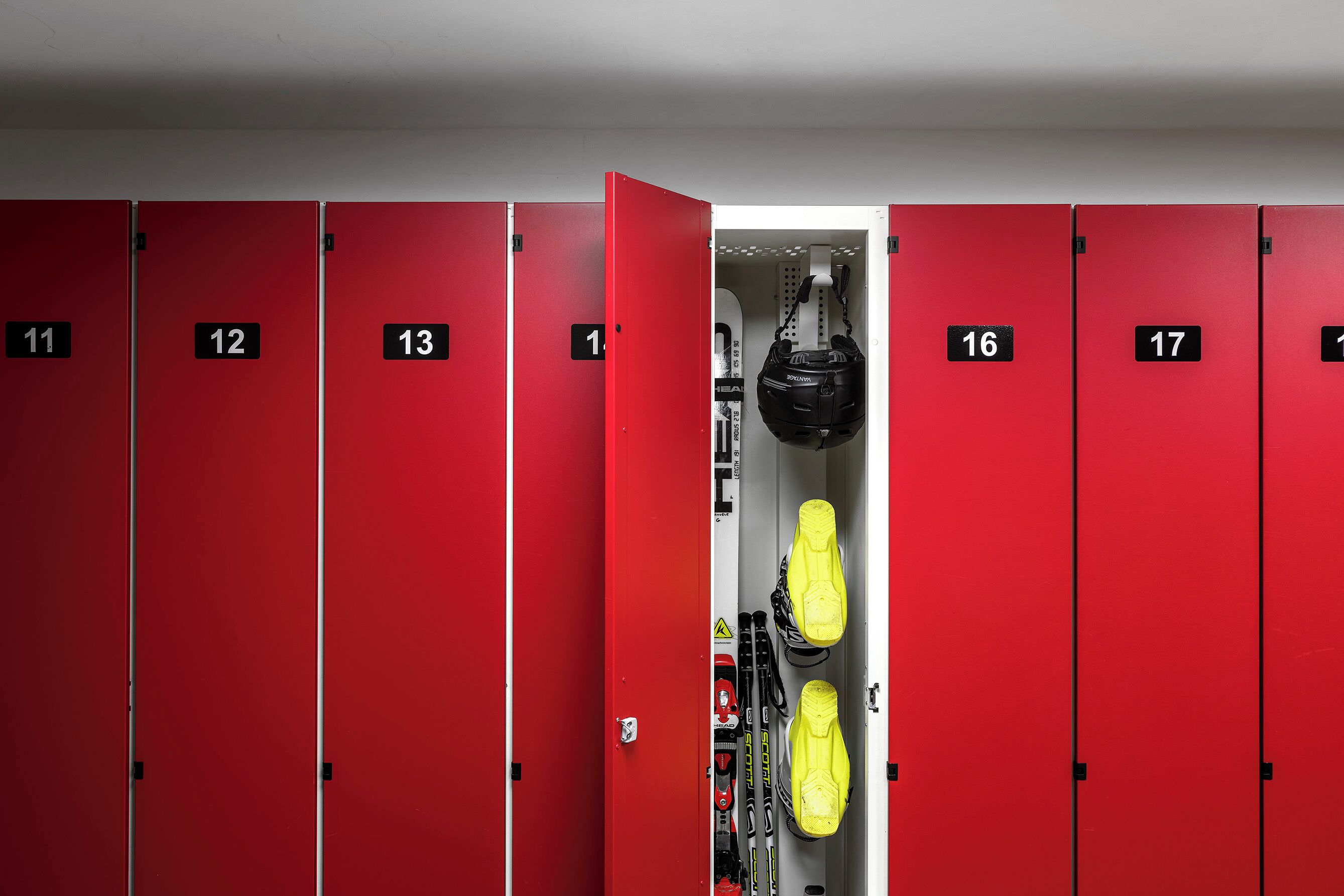 Eine Reihe von roten Umkleidefächern mit den Nummern 11 bis 17, wobei ein zentrales Fach gelbe Schuhe und einen schwarzen Helm enthält.