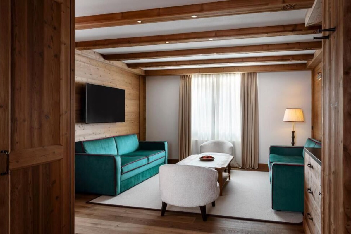 Una habitación con techo de madera, un sofá color turquesa, un sillón blanco, una mesita y un televisor montado en la pared.