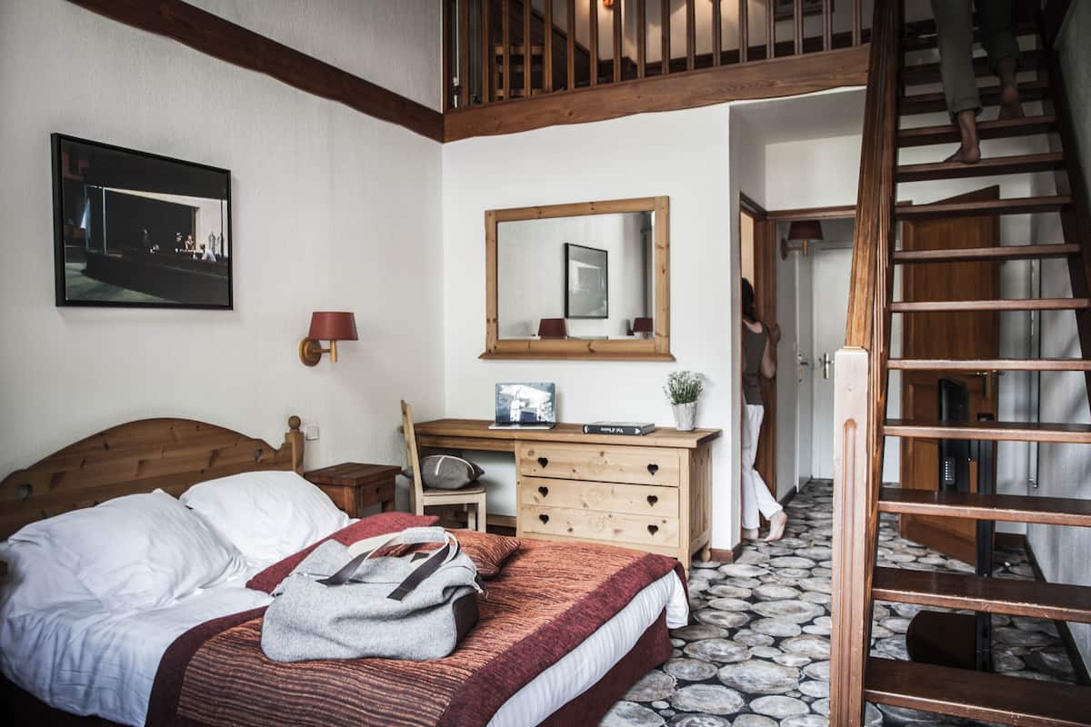 A bedroom with a wooden bed, a dresser, a mirror, and a staircase.