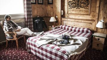 A cozy room with a checkered bedspread, a wooden headboard, a nightstand with a lamp, and a chair with a blanket.