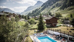 A mountain resort with a swimming pool, lounge chairs, and a view of the surrounding mountains.