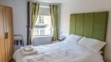 A neatly made bed with white linens, a green headboard, and a window with curtains.