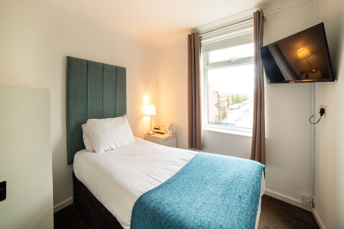 Une chambre d’hôtel avec un lit, une table de chevet, une lampe, un téléviseur fixé au mur et une fenêtre avec des rideaux.