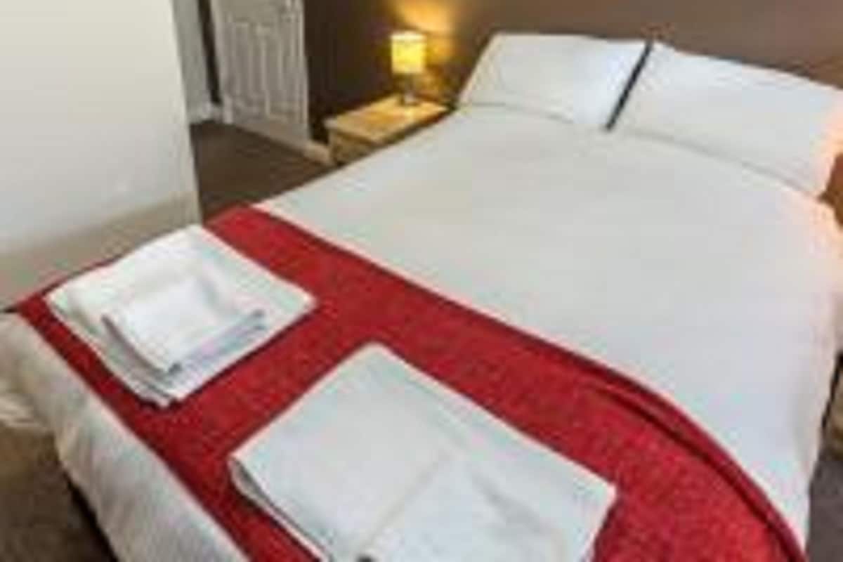 Une chambre d’hôtel avec un lit bien fait, une table de chevet avec une lampe et une porte visible au fond.