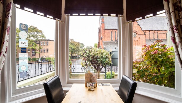 A dining area with a table and chairs, a view of a church, and a flower box on the windowsill. - The Douglas Hotel (Hartlepool)