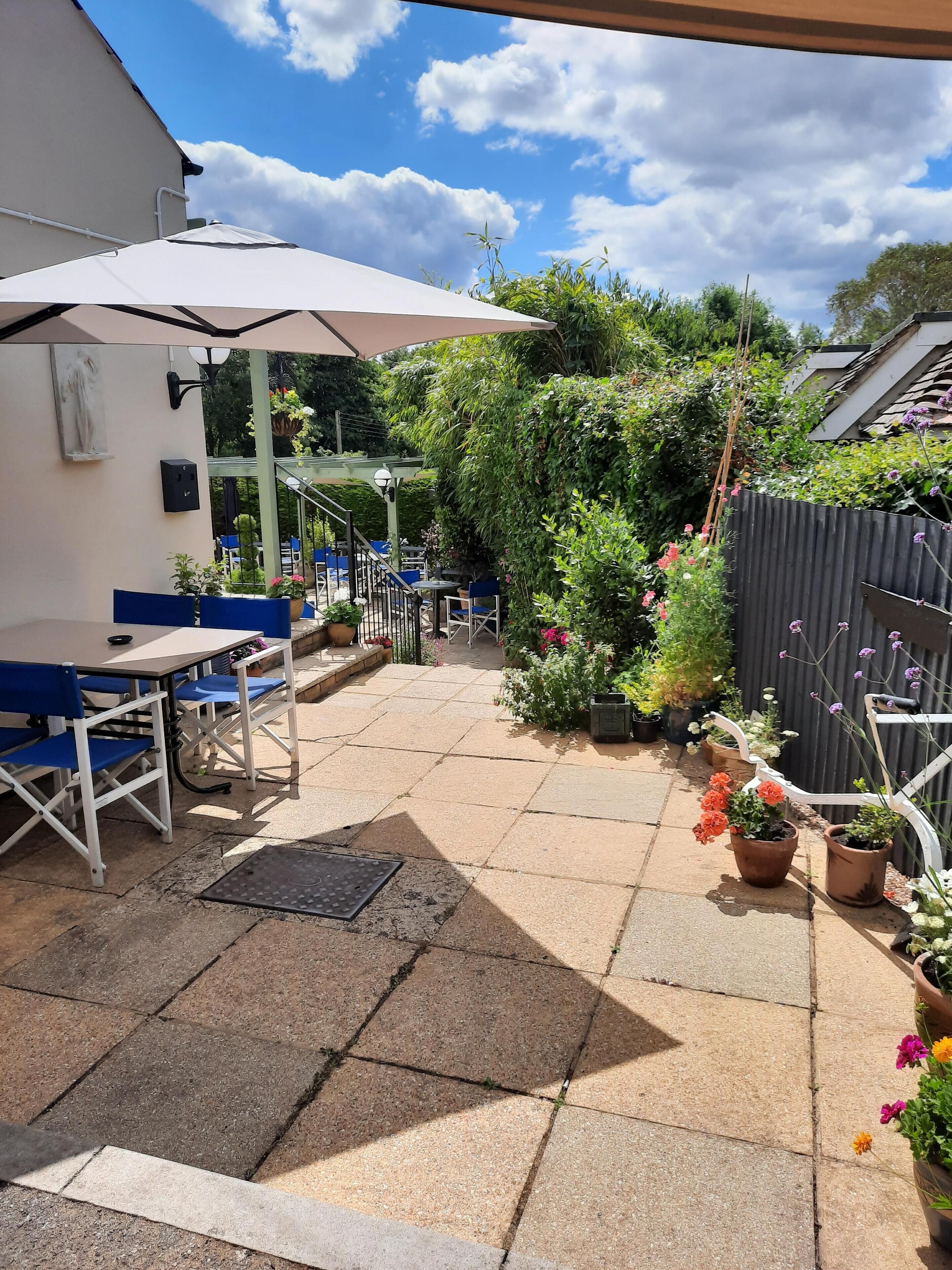 A patio area with outdoor seating, potted plants, and a pergola providing shade.