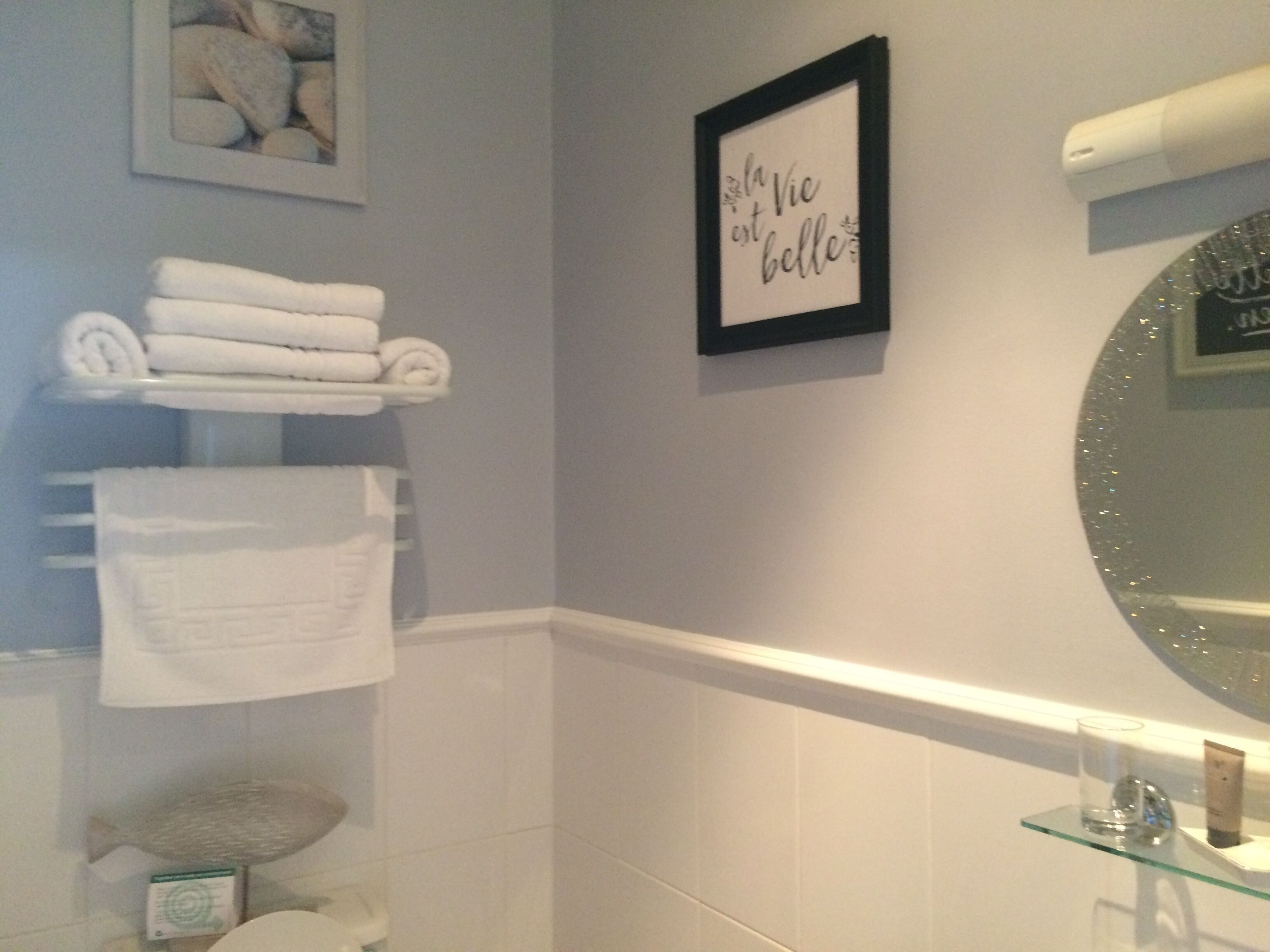 A bathroom with a towel rack, a framed sign, a mirror, and a glass shelf with toiletries.