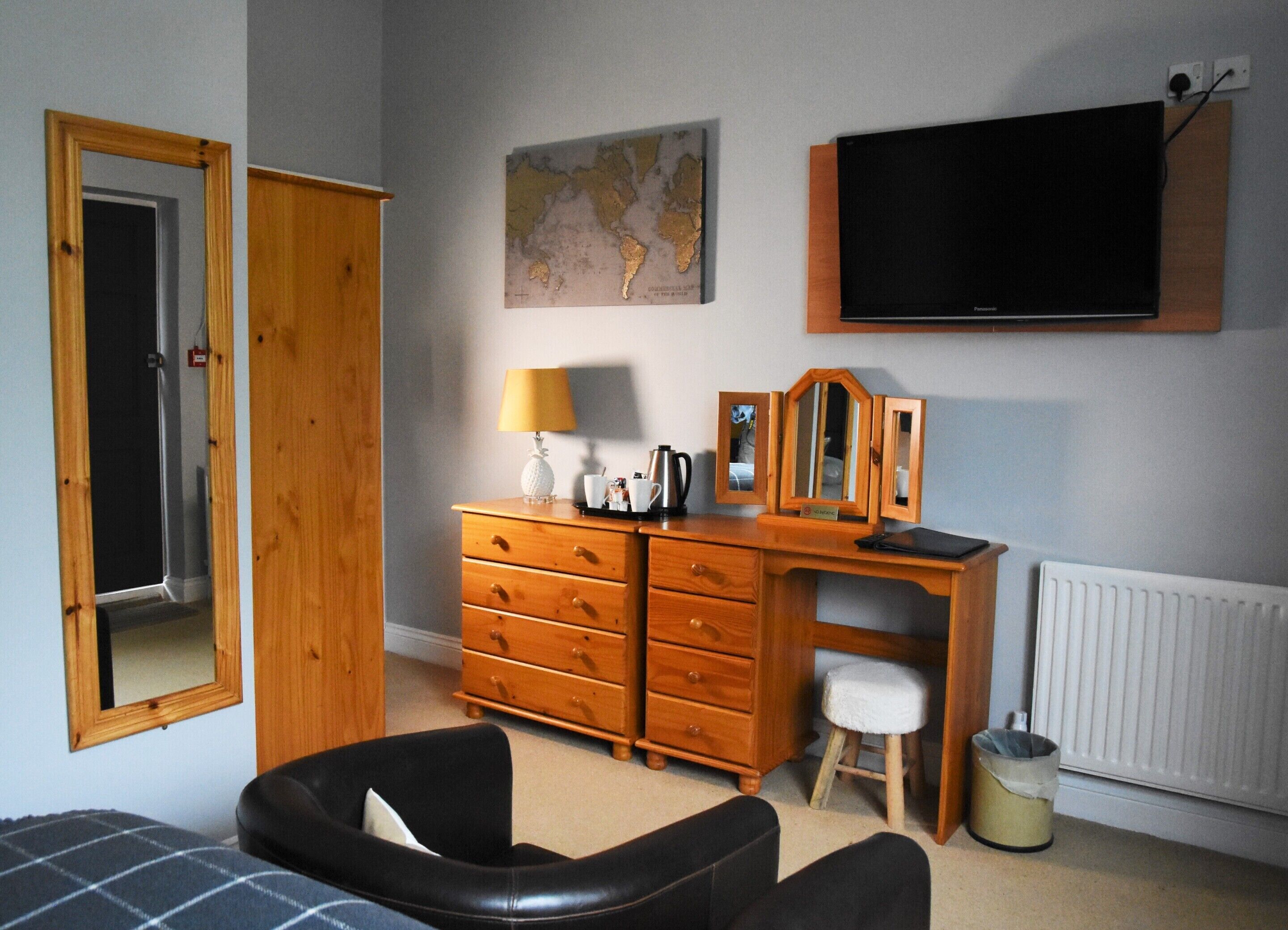 Un dormitorio con un aparador de madera, un escritorio, una silla, una cama, un televisor, un mapa en la pared y un radiador.