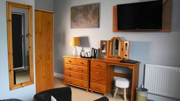 Un dormitorio con un aparador de madera, un escritorio, una silla, una cama, un televisor, un mapa en la pared y un radiador.