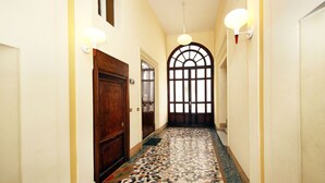 A hallway with a patterned floor, wooden doors, and wall-mounted lights. - Tibullo Guesthouse (Rome)