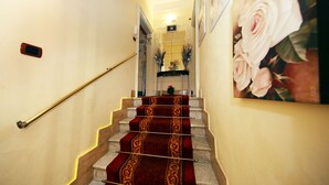 A staircase with a red carpet and a handrail, leading to a room with a bed and a nightstand. - Tibullo Guesthouse (Rome)