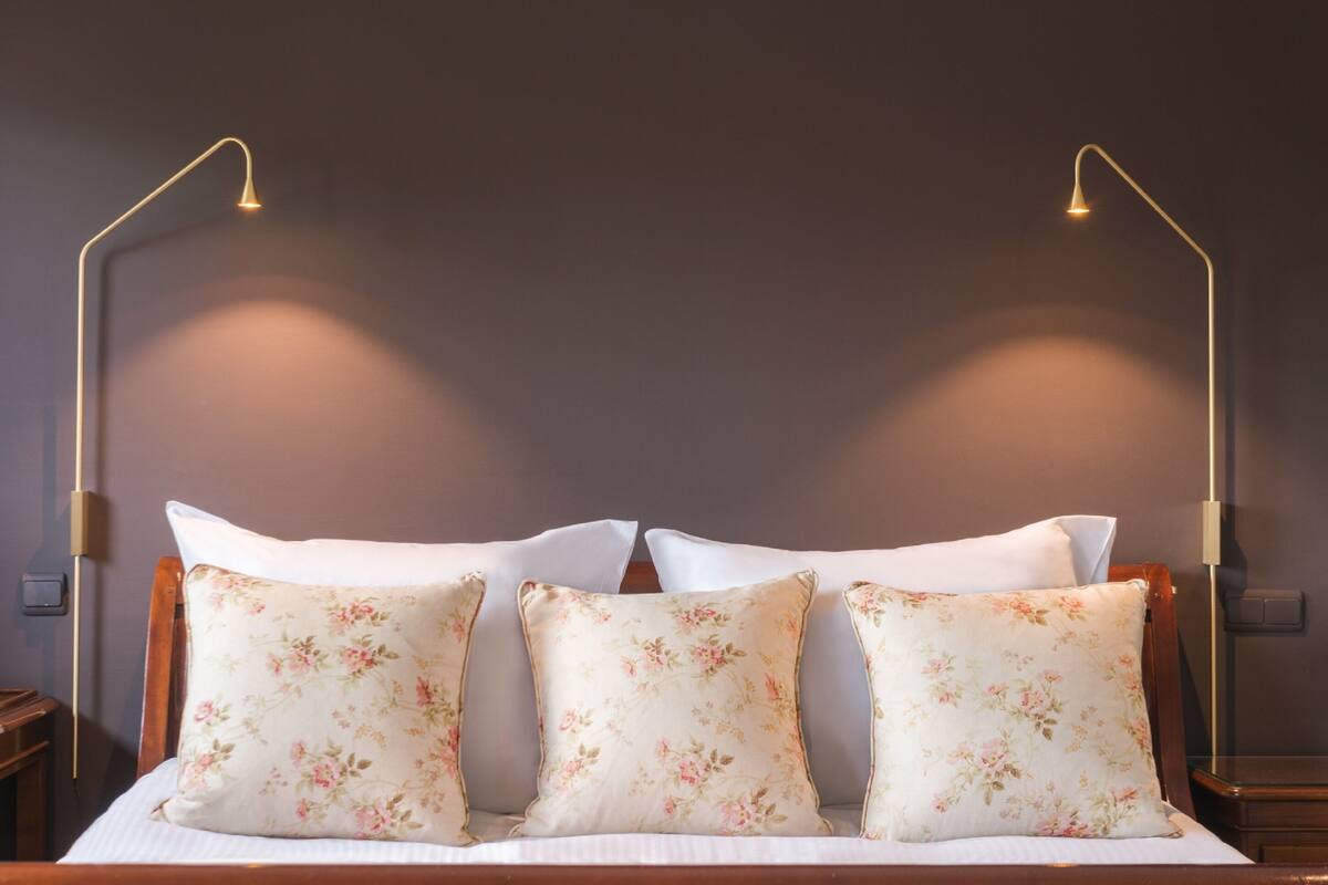 A bed with floral-patterned pillows, a wooden headboard, and two wall-mounted lamps.