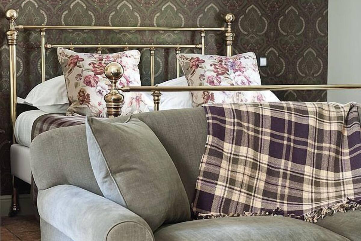A room with a grey sofa, a plaid throw blanket, and a bed with floral pillows.