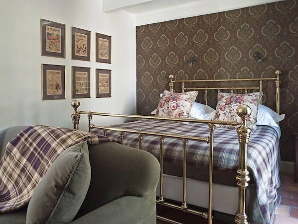 A bedroom with a four-poster bed, a green armchair, and a patterned wallpaper.