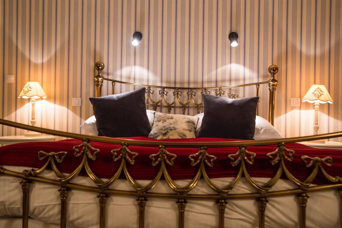 A bed with a red bedspread, two pillows, and a gold-framed headboard.